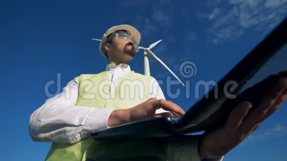 男性专家正在天空和风车的背景下使用笔记本电脑视频的预览图