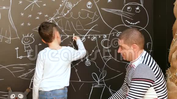 男孩和父亲用粉笔在墙上画一幅圣诞节主题的画视频的预览图