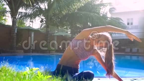 年轻女子坐在瑜伽姿势下双手弯曲曲从泳池边离开视频的预览图