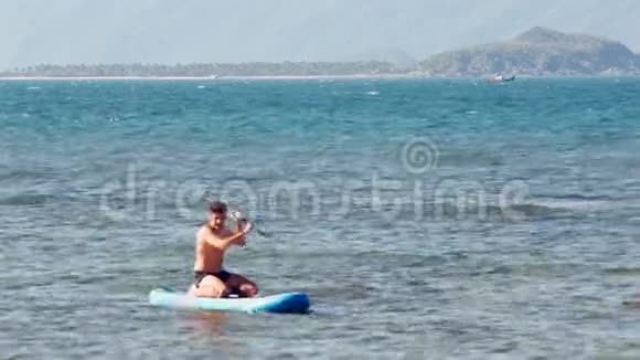 强壮的人坐在漂浮在大海上的桨板上视频的预览图