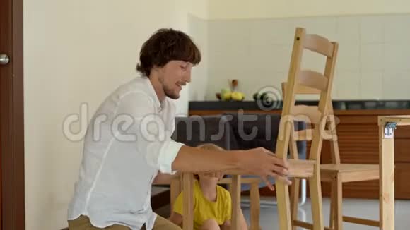 父子俩用小零件组装木制家具整理完一张椅子后一个人把他的儿子放在椅子上视频的预览图