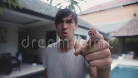 愤怒的男人用手指威胁并在他院子里的房子的背景上咄咄逼人地尖叫威胁视频的预览图