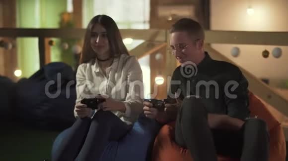 年轻人和女人在咖啡馆里坐在舒适的椅子上玩电子游戏可爱的一对夫妇有约会玩得开心视频的预览图