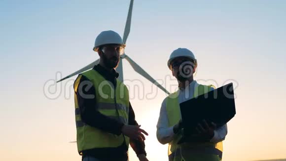 两位男性专家正在风车前进行讨论清洁环保的能源理念视频的预览图