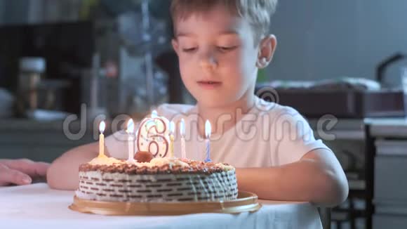 男孩坐在厨房的桌子上在生日蛋糕上吹蜡烛许愿视频的预览图