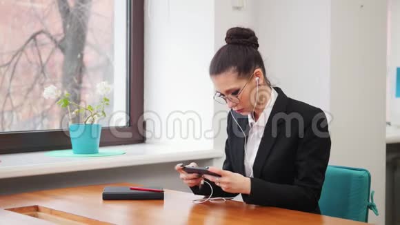 商业概念一个戴着耳机的女人坐在桌子旁用手机玩游戏视频的预览图