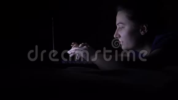 迷人的年轻快乐的女人在晚上躺在床上时使用移动电脑隔离灯4K视频的预览图