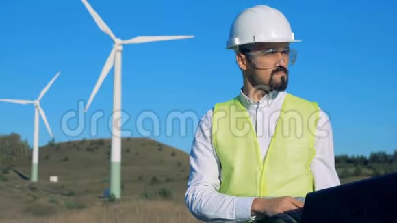 一位工程师正在风车前操作一台笔记本电脑清洁环保的能源理念视频的预览图