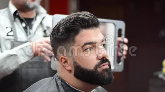 理发后一个英俊的留胡子的男人在理发店照镜子视频的预览图