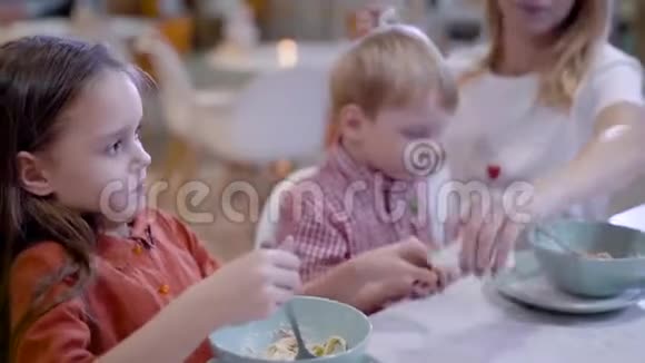 咖啡馆里美丽的年轻母亲一个女人用意大利面喂儿子她女儿旁边吃她自己的菜视频的预览图
