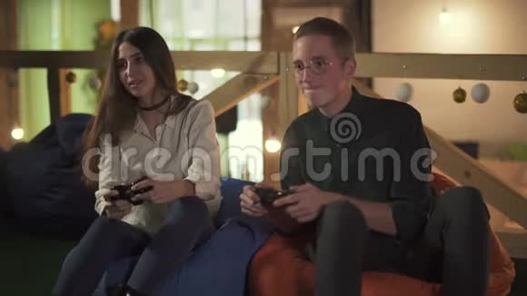 年轻人和女人在咖啡馆里坐在舒适的椅子上玩电子游戏可爱的一对夫妇有约会玩得开心视频的预览图