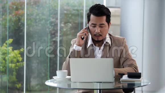 穿西装的沮丧男人在智能手机上说话用笔记本电脑视频的预览图