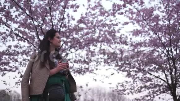 年轻女子走在公园里樱花盛开喝着纸杯里的咖啡做梦视频的预览图