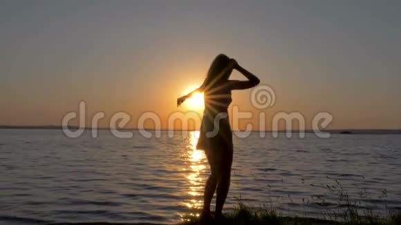一个幸福的女人美丽而优雅地在海上夕阳下翩翩起舞的剪影视频的预览图
