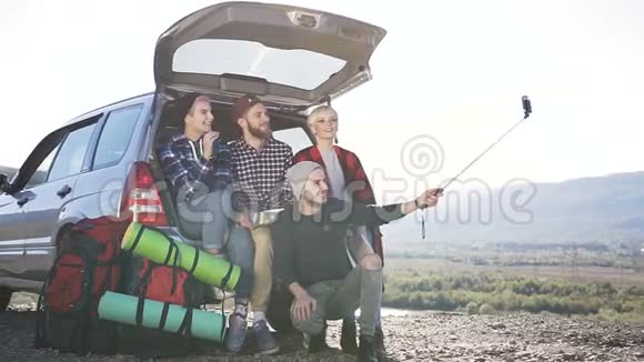 四个年轻人在智能手机上自拍在山景背景下靠在SUV车箱上视频的预览图