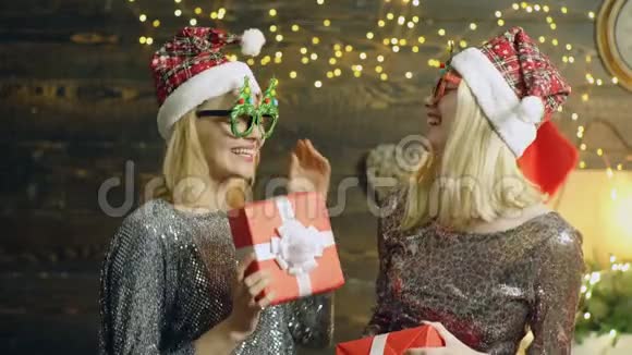 戴着眼镜和帽子的疯狂新年女孩带着礼品盒跳舞两个金发女郎穿着银色迷人的礼服和新年视频的预览图