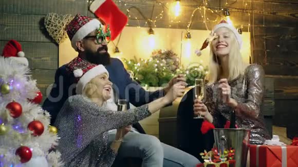 穿着西装戴着新年礼帽的大胡子男人正在和两个女孩一起玩她们点燃孟加拉灯在香槟酒上喝香槟视频的预览图
