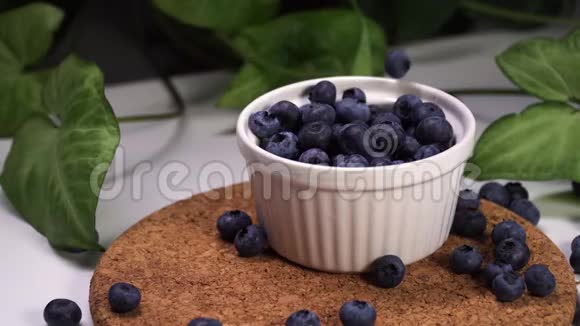 新鲜的蓝莓落在白色的碗里背景中绿色植物的电影景观视频的预览图