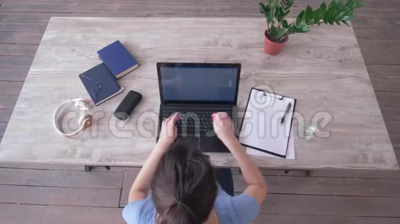自由职业者女孩在笔记本电脑键盘上输入文字并在桌旁的剪贴板上写笔记视频的预览图