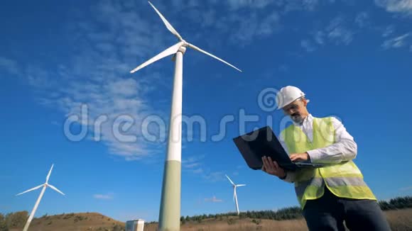 功能强大的风力涡轮机塔和一个能源工人站在他们旁边与笔记本电脑清洁环保能源视频的预览图