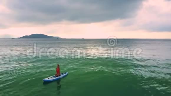 女孩坐在划桨船上靠在粉红色的天空上视频的预览图