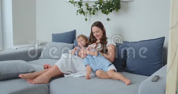 妈妈抱着两个小儿子在客厅的沙发上看电视家庭看电视视频的预览图