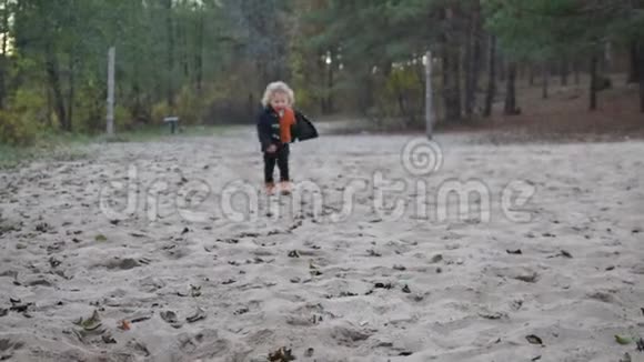 一个卷发的小男孩穿过沙滩跑到玩具旁视频的预览图