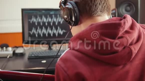 一个戴着耳机的人坐在录音室的电脑旁录制一首歌视频的预览图