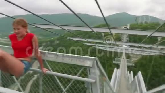 在绿色山谷的背景下穿着红色T恤的金发美女在高山桥上向她的红发姐姐摆姿势视频的预览图