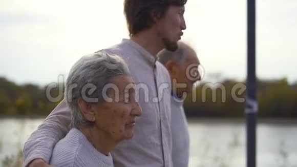 一个年轻人和他的祖父母在河边的人行道上散步时的慢镜头视频的预览图