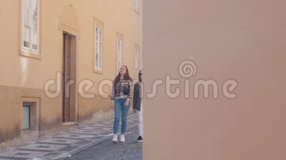 两个年轻的女旅行者走在狭窄的街道上交谈视频的预览图