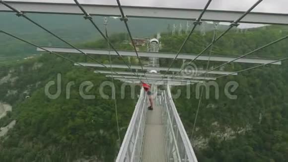穿着红色T恤的年轻金发女郎从吊桥往下看吐在那里视频的预览图
