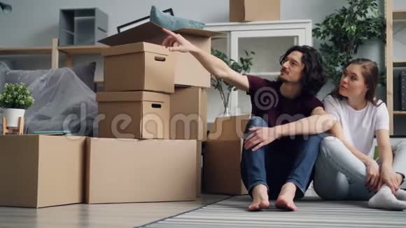 搬迁期间年轻妇女与丈夫坐在地板上拿着箱子说话视频的预览图