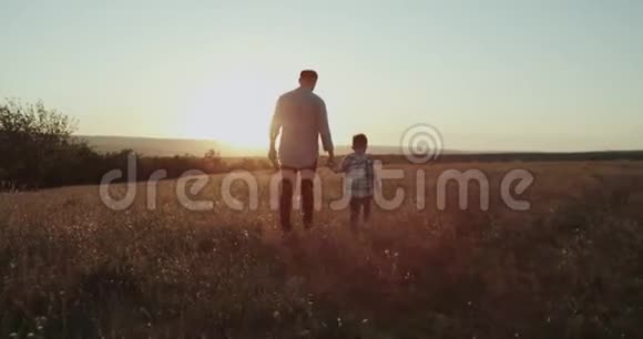 爸爸带着他的男孩在夕阳下穿过田野爸爸拿着网球拍在红色史诗上拍摄4k视频的预览图