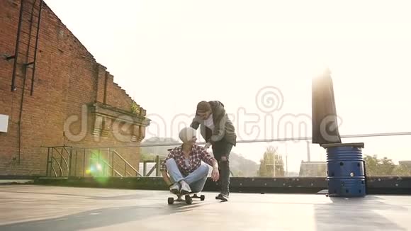 在日落时分海普斯特女孩正和她的男朋友一起在屋顶上的滑板上玩耍帅哥小伙子视频的预览图