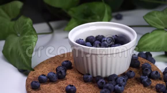 美味的蓝莓落在白色的碗里背景中绿色植物的电影景观视频的预览图