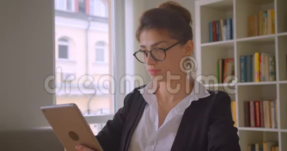 年轻漂亮的白种人女商人在眼镜上用平板电脑拍摄特写镜头并显示绿色的彩色屏幕视频的预览图