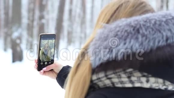 一个在雪地森林里带着手机的女孩在倒影中快乐地玩着视频的预览图