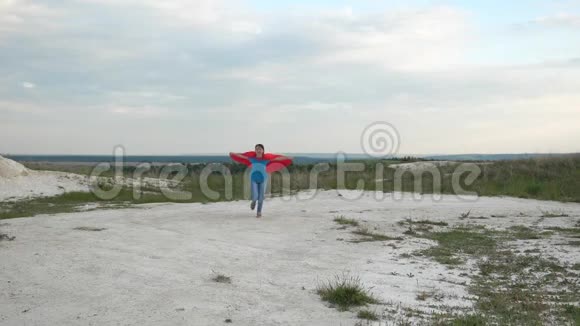 快乐女孩超级英雄穿着红色斗篷在蓝天面前跑过田野微笑着慢动作年轻女孩梦想视频的预览图