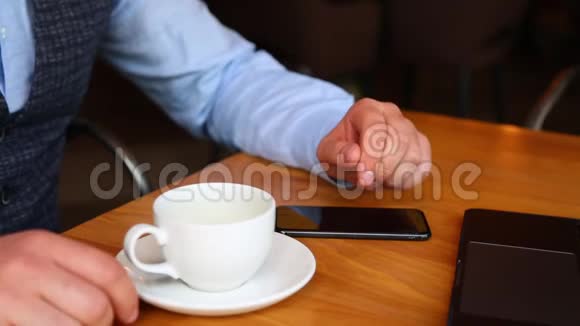 在咖啡馆里有笔记本电脑的商人喝咖啡和使用智能手机视频的预览图
