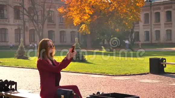 年轻迷人的女学生坐在大学广场上在阳光明媚的温暖日子里自拍视频的预览图