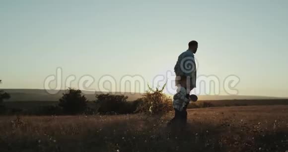 爸爸带着三岁的男孩在夕阳西下的田野里玩着一个网球拍视频的预览图