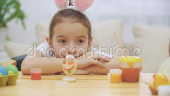 疲倦可爱的女孩躺在桌子上看着她的创作彩色有趣的复活节彩蛋视频的预览图