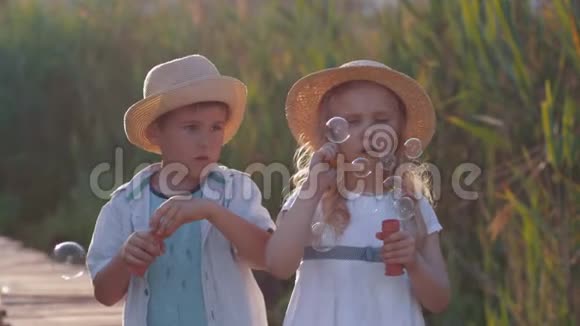 孩子们的娱乐活动快乐的小朋友男孩和女孩戴着草帽在阳光下吹泡泡视频的预览图