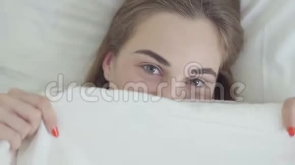描绘了一个可爱的年轻快乐的白种人女人两只不同颜色的眼睛躺在床上用一双眼睛遮住她的脸视频的预览图