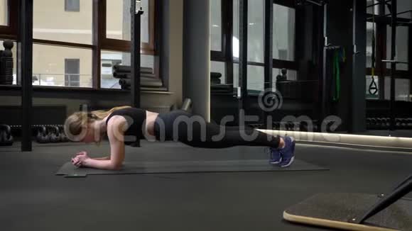 年轻的运动女孩站在木板上手机躺在健身房附近视频的预览图