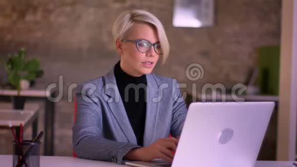 戴眼镜的中年短发女商人在办公室里用笔记本电脑在电玩上说话的肖像视频的预览图