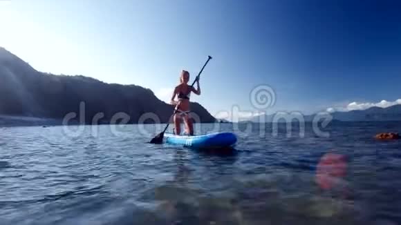 穿比基尼的苗条女孩在开阔的海洋上划桨视频的预览图