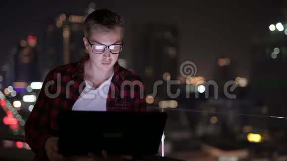 年轻快乐的嬉皮士男子用笔记本电脑对城市夜景视频的预览图