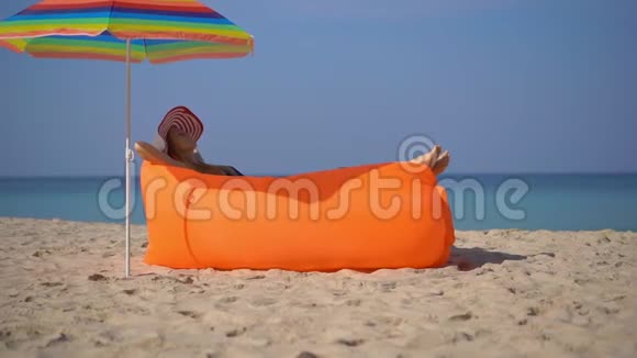 一名年轻女子躺在一张充气沙发上的热带海滩上的超慢镜头暑假概念视频的预览图